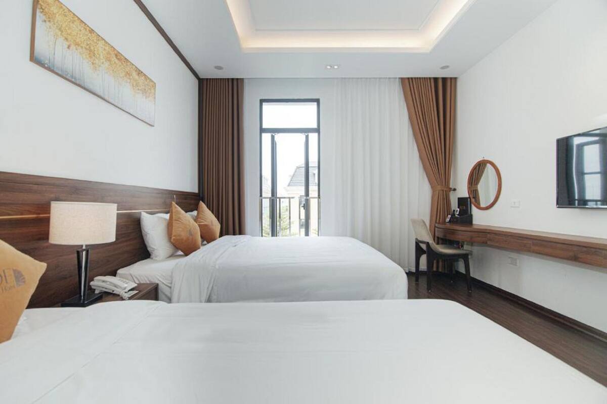 A hotel room with two beds, a desk, a chair, a large window, and a ceiling light.