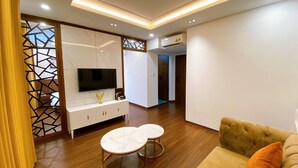A modern living room with a TV, white furniture, and a wooden floor. - JADE HA LONG HOTEL (Bai Chay)