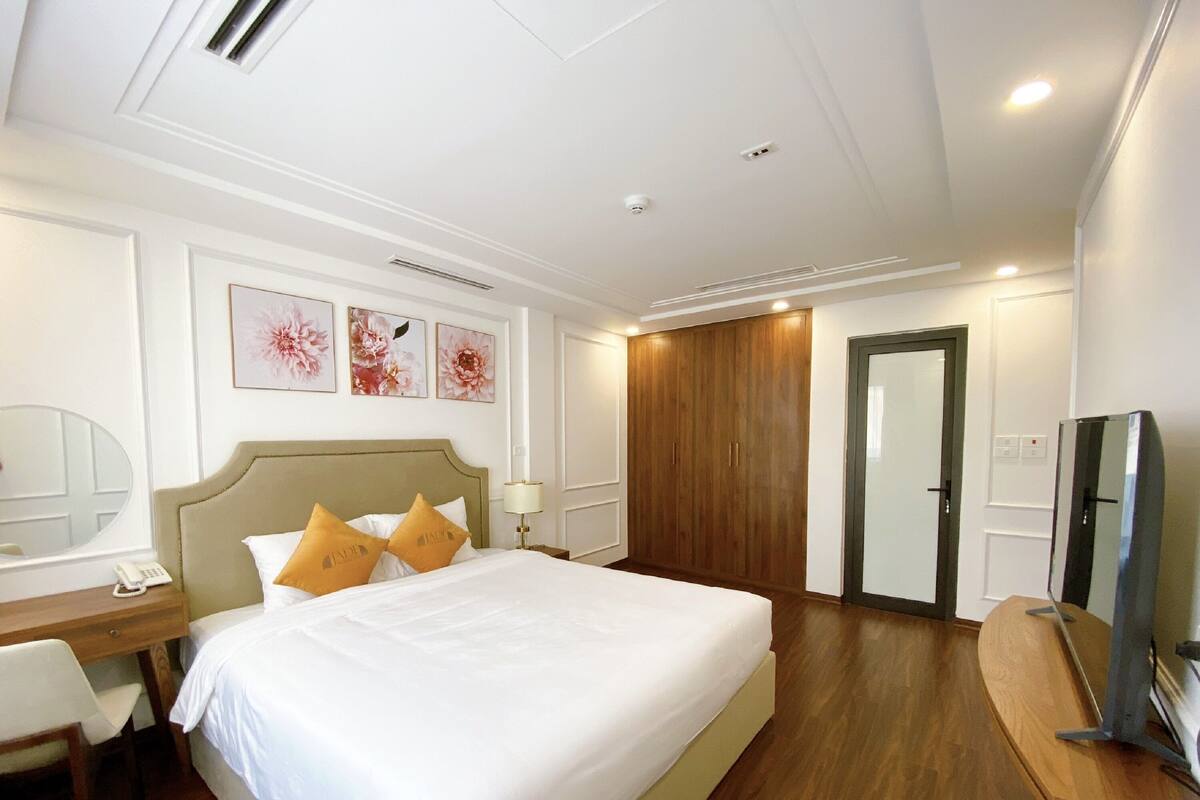 A hotel room with a large bed, a desk with a chair, a mirror, and a television on a wooden stand.