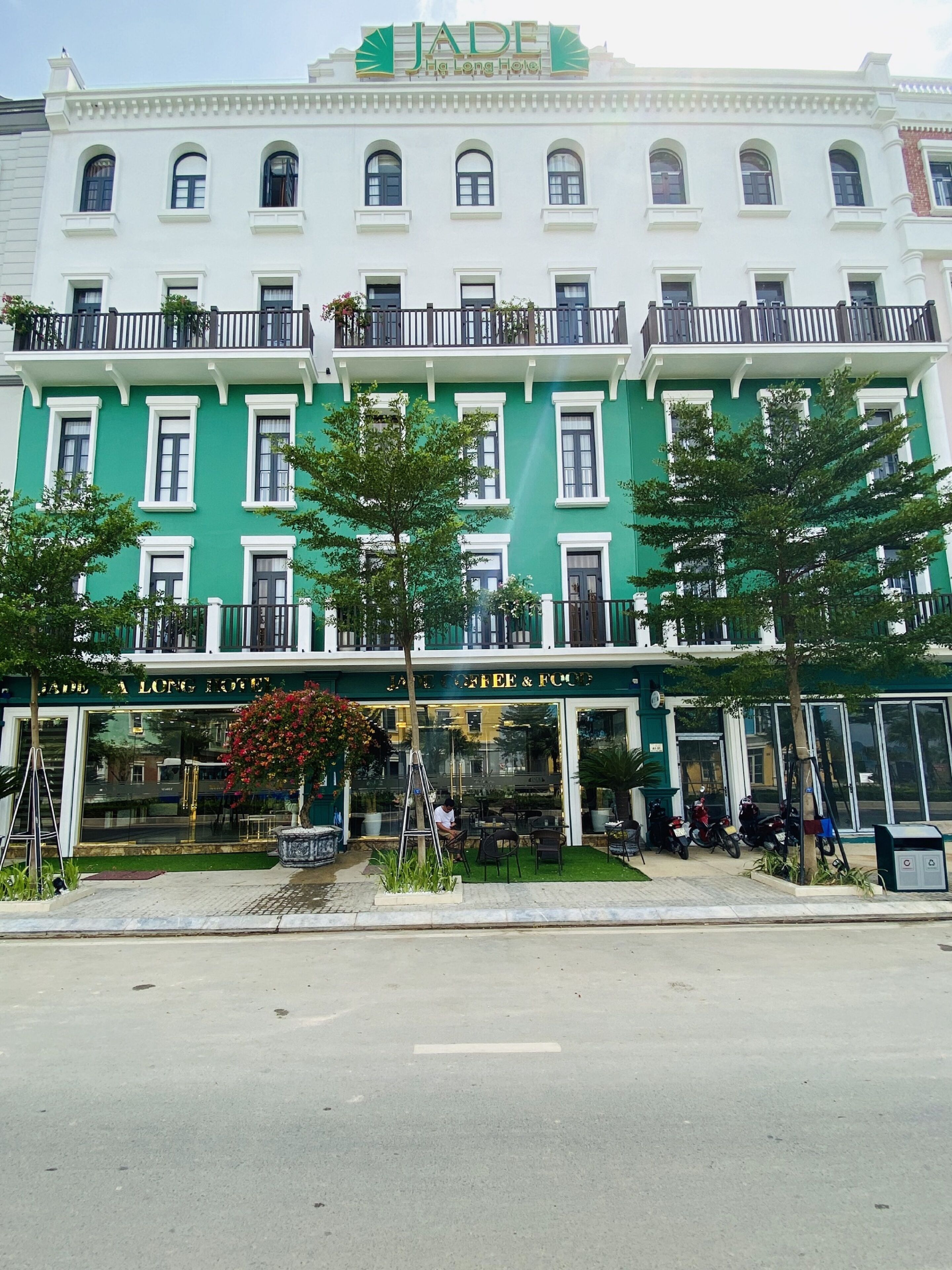 A multi-story building with a green facade, multiple balconies, and a ground-level coffee shop.