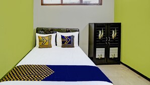A bed with a white and blue bedspread, two pillows with geometric patterns, and a dark-colored wardrobe with a window.