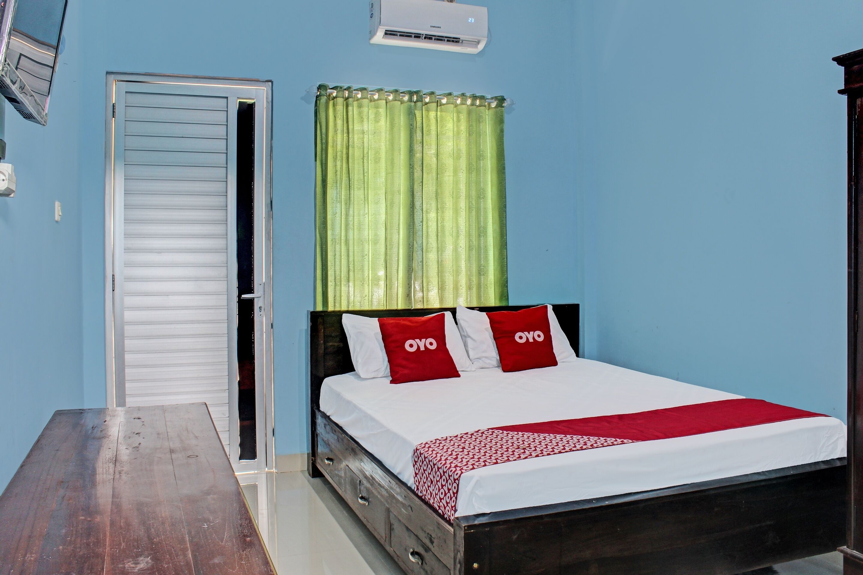 A bedroom with a wooden bed, a white headboard, a green curtain, and a white door.
