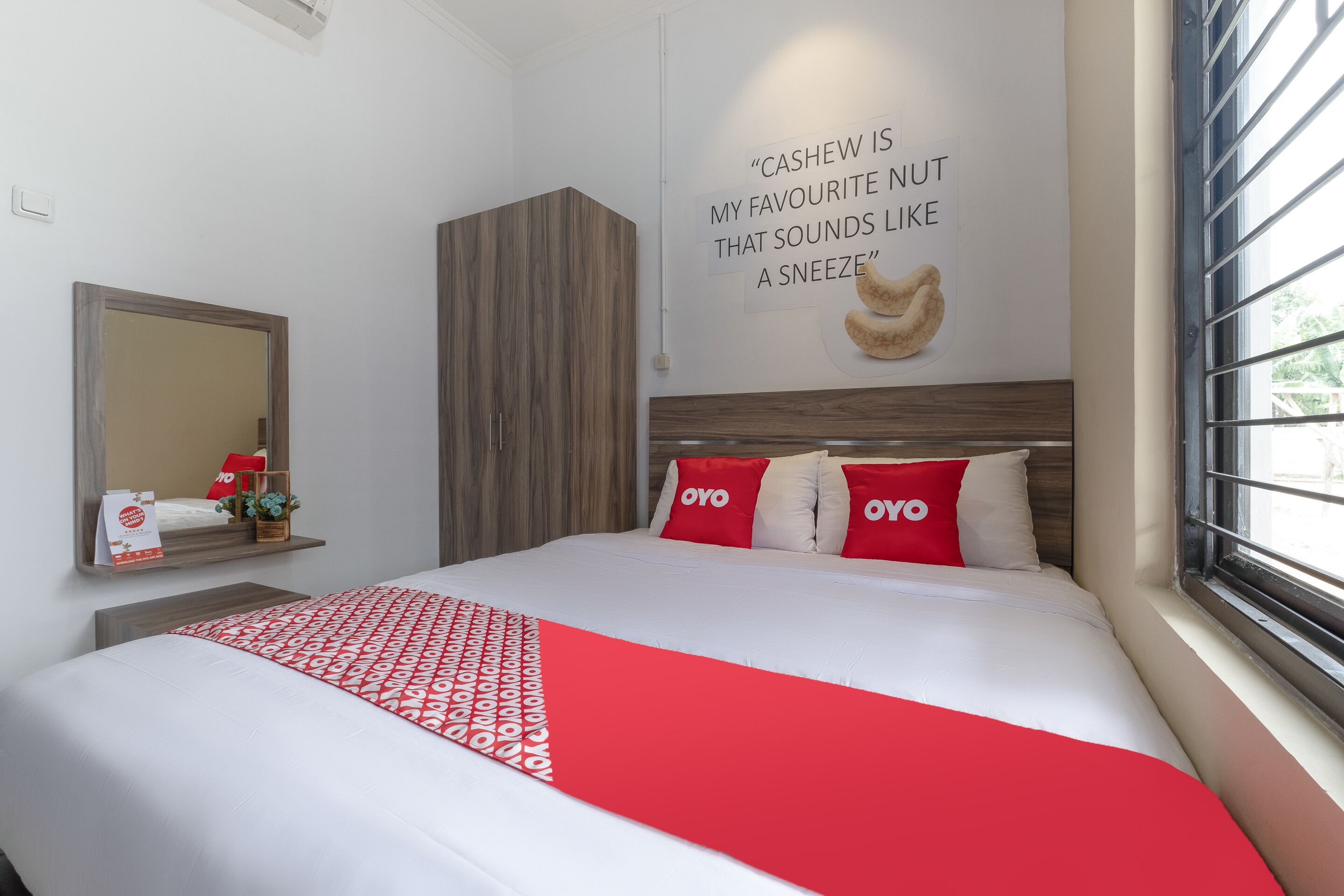 A modern hotel room with a large bed, a wooden headboard, a wall-mounted mirror, and a window with blinds.