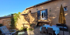 A building with a stone facade, a balcony with a metal railing, and outdoor seating with tables and chairs. - Gîte Provence Piscine Luberon - Domaine ARTEMISS (APT)