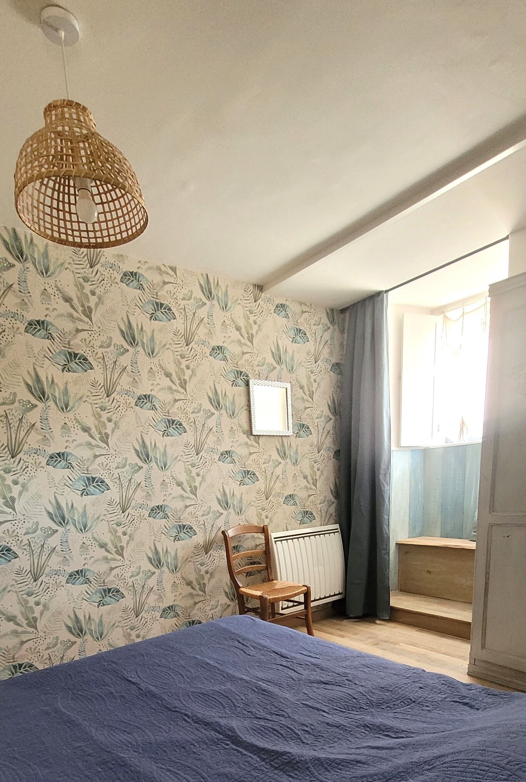 Ein Schlafzimmer mit Bett, Sessel, Heizkörper und einem fenster mit Vorhängen.