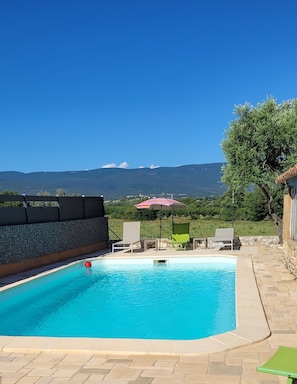 Une piscine dotée de chaises longues et d’un parasol, entourée d’un mur de pierre et offrant une vue sur les montagnes.