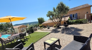 Une terrasse avec des meubles d’extérieur, une piscine et une maison avec un toit en tuiles.