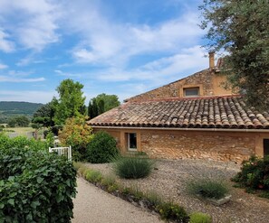 A stone house with a tiled roof, surrounded by a gravel path and greenery. - Gîte Provence Piscine Luberon - Domaine ARTEMISS (APT)