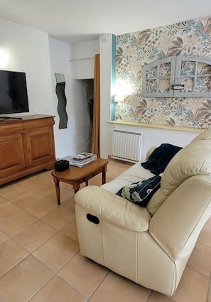 Un salon comprenant un canapé, un téléviseur, un meuble en bois et un mur orné d’un motif décoratif.