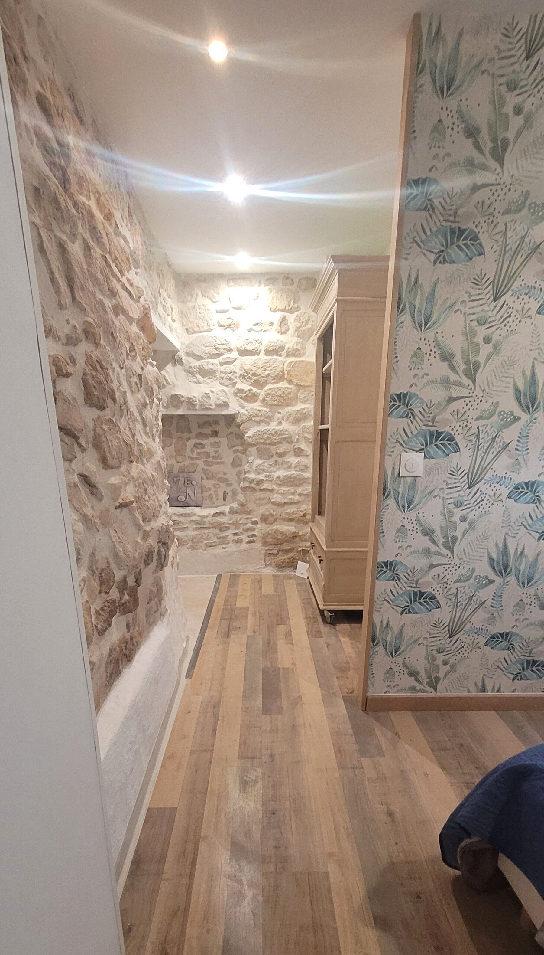 Ein schmaler Korridor mit Steinwänden, Holzboden und einem Schrank.