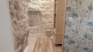 Un couloir étroit aux murs de pierre, au plancher en bois et où se trouve un meuble.