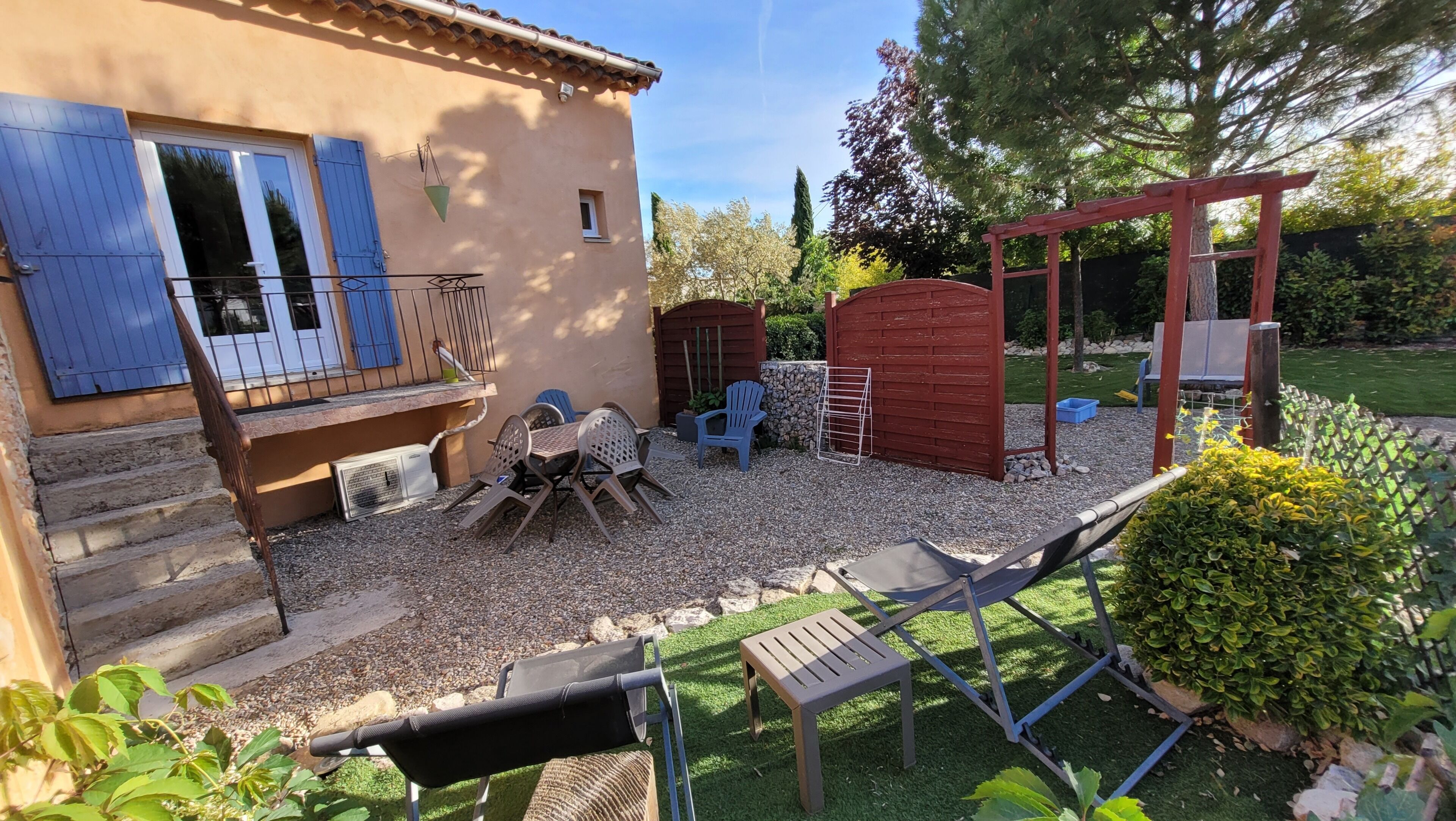 Un espace patio aménagé avec du mobilier d’extérieur, une petite table et une structure en bois rouge.