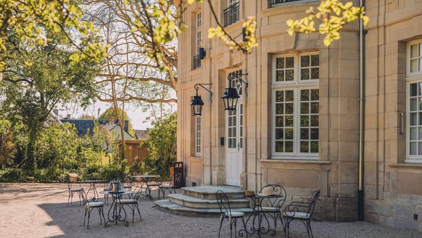 Une cour avec des sièges en plein air et un bâtiment aux murs et aux fenêtres en pierre.