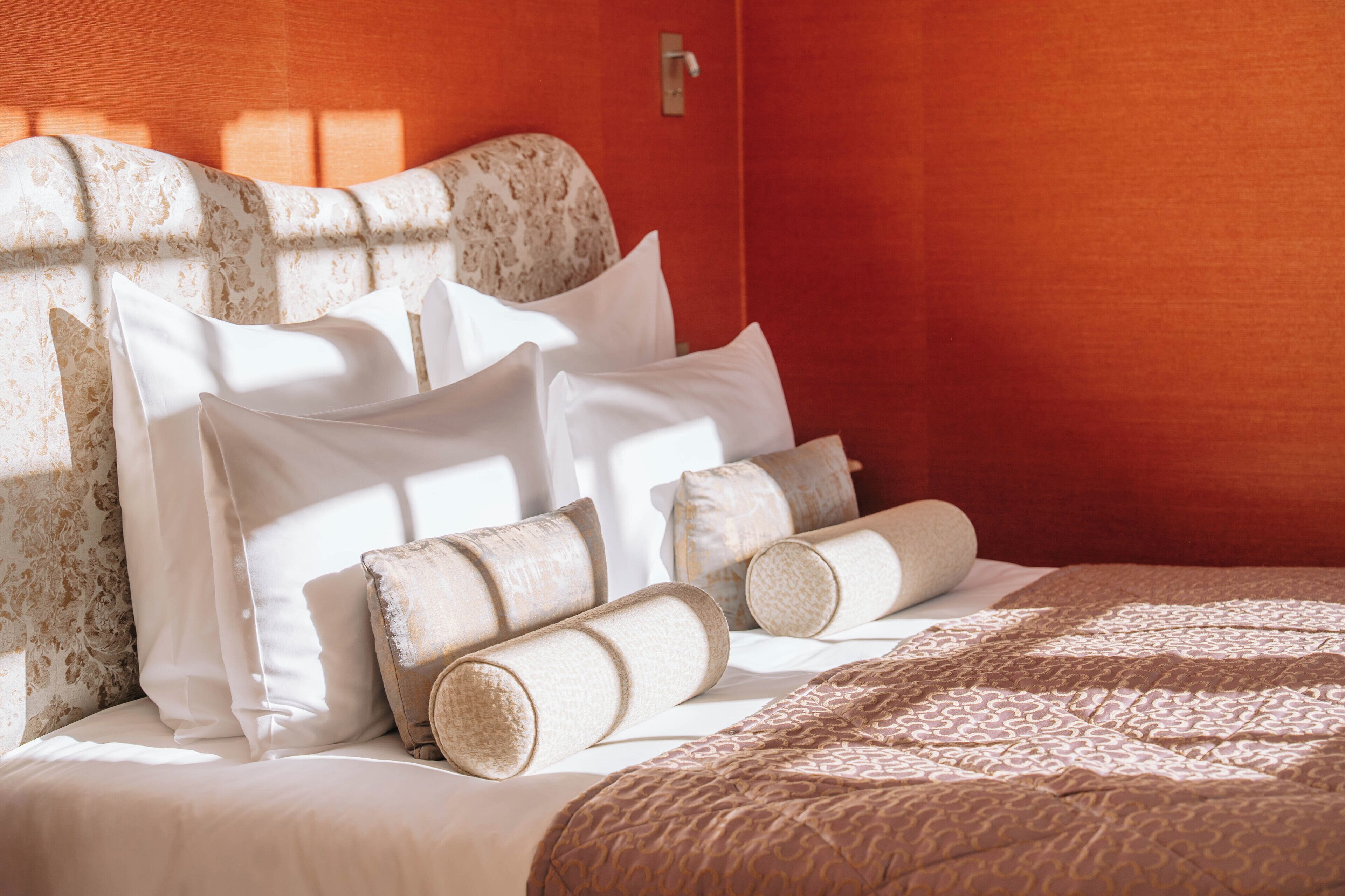 A neatly made bed with white linens and rolled towels, a patterned quilt, and a headboard with a floral design.