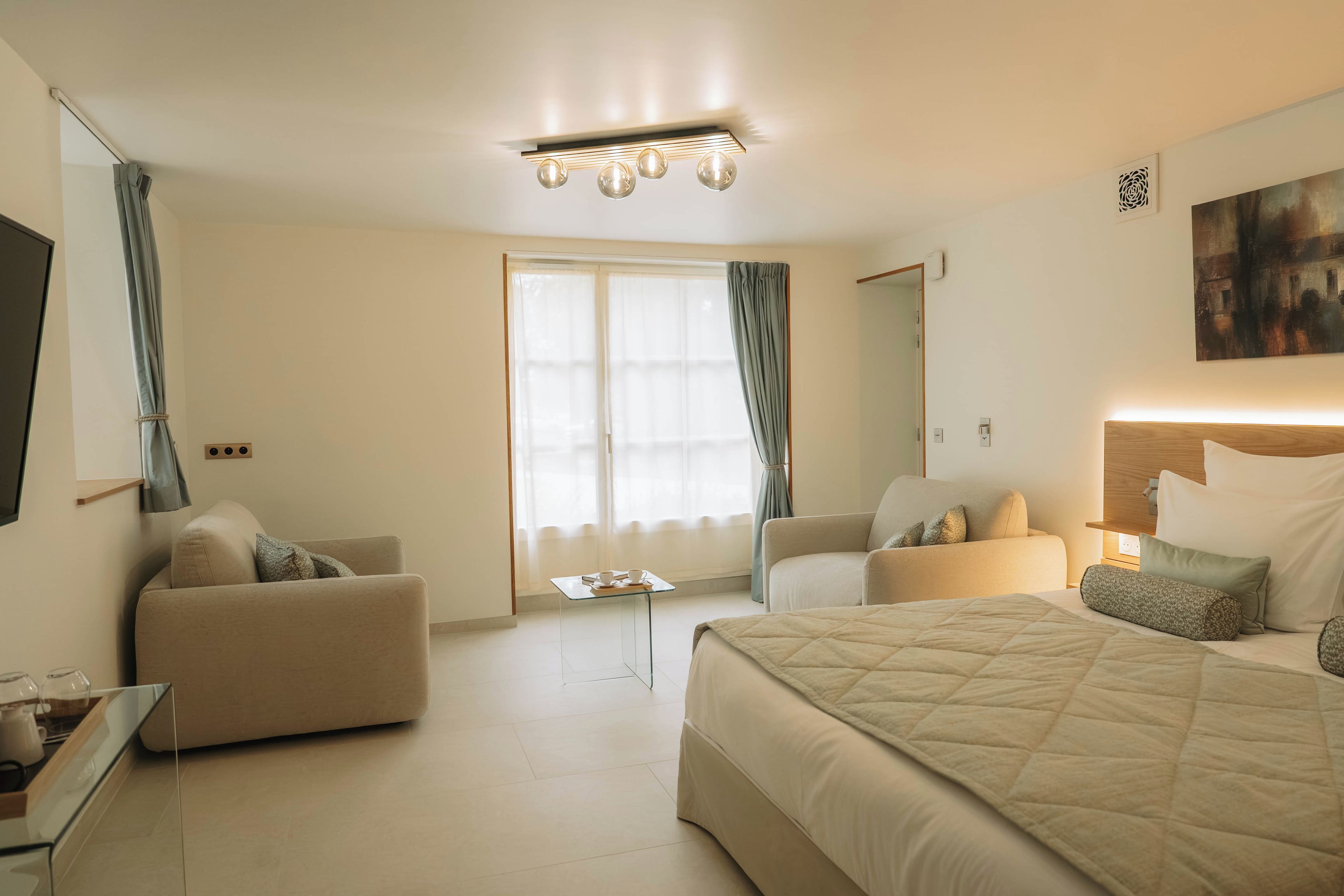 Una habitación de hotel con una cama, dos sillones, una mesita, un televisor y un cuadro en la pared.