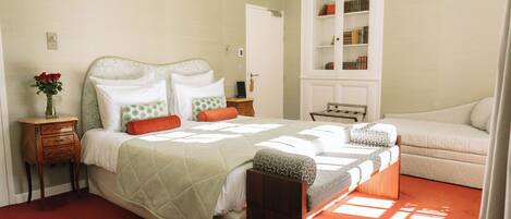 A bedroom with a bed, bedside tables, a nightstand, a bookshelf, and a window.