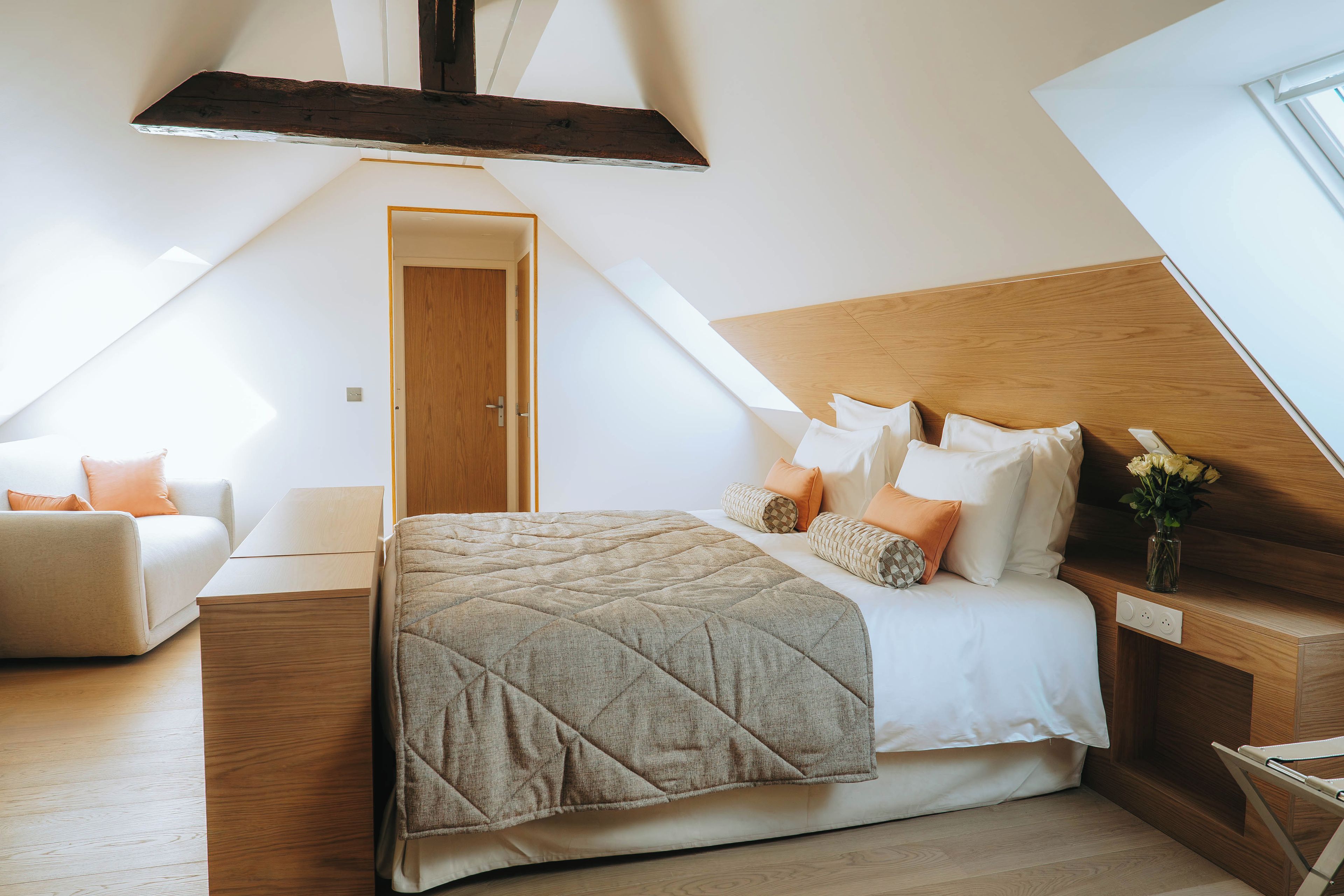 A bedroom with a sloped ceiling, a bed with a quilted bedspread, a wooden headboard, and a nightstand with a vase of flowers.