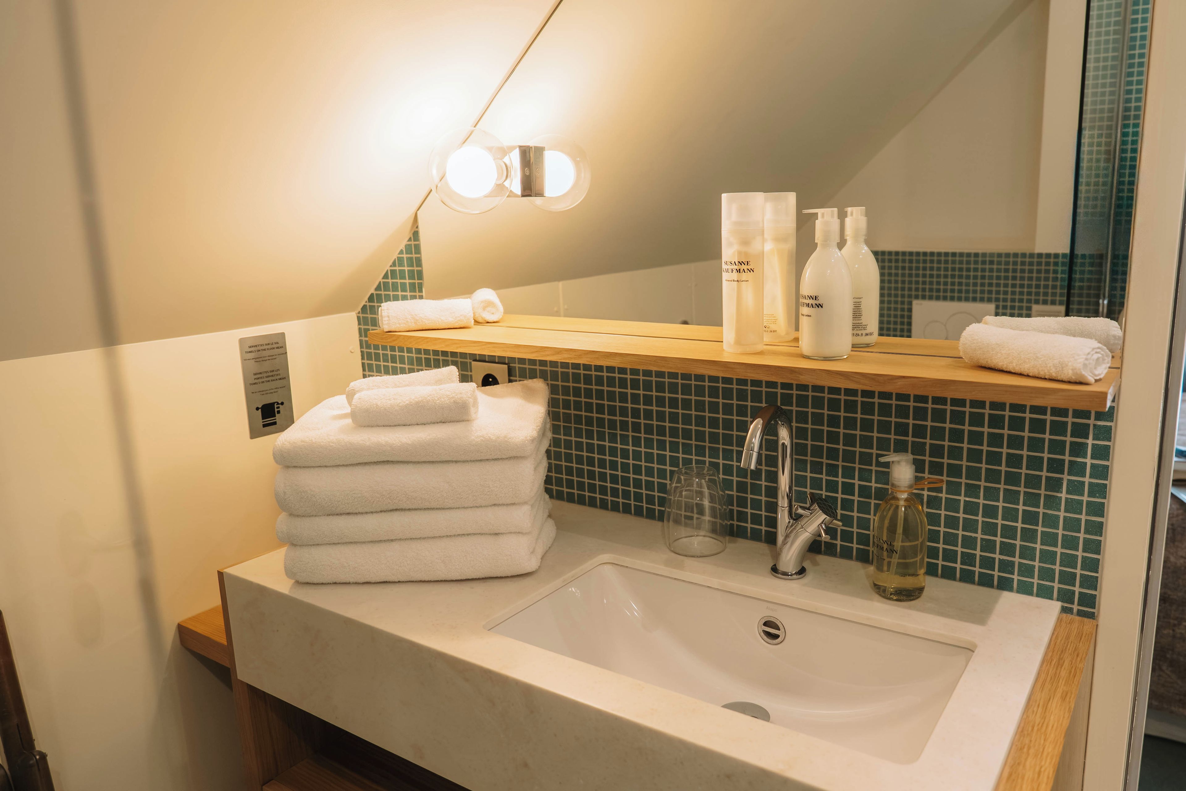 Baño con lavamanos, espejo, toallas y artículos de aseo.
