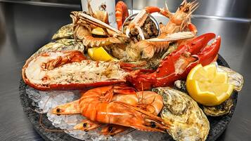 A seafood platter with various shellfish and a bottle of wine on a black slate plate.
