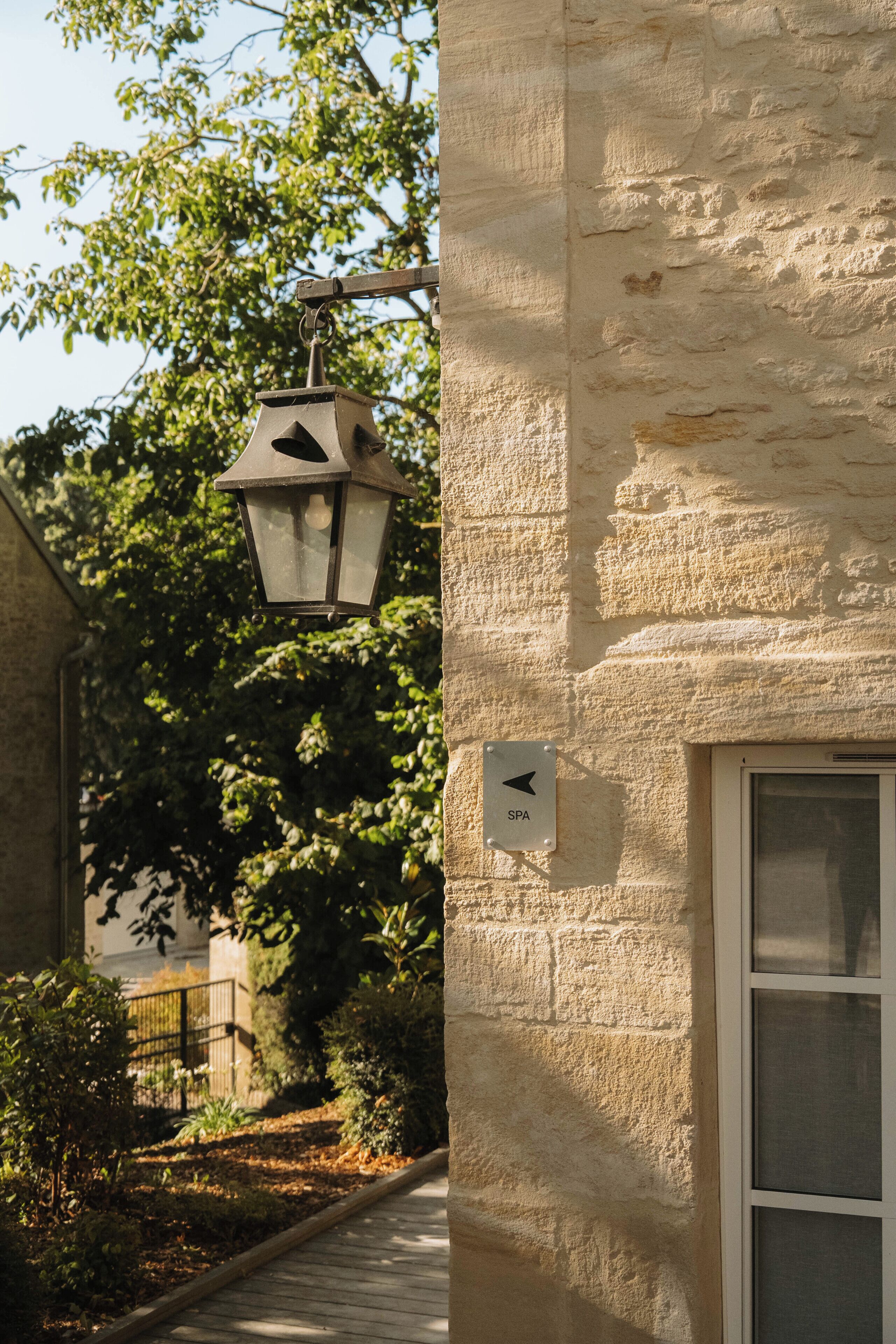 A stone building with a lantern hanging from a metal bracket, a door with a sign indicating a spa, and a window with blinds.