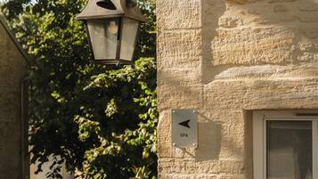 A stone building with a lantern hanging from a metal bracket, a door with a sign indicating a spa, and a window with blinds.