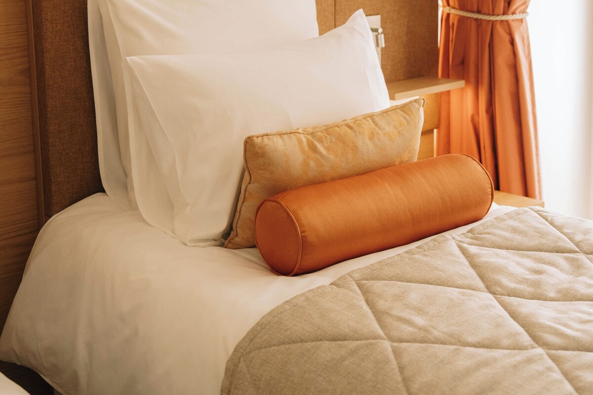 A neatly made bed with a quilted cover, two pillows, and a decorative orange pillow.