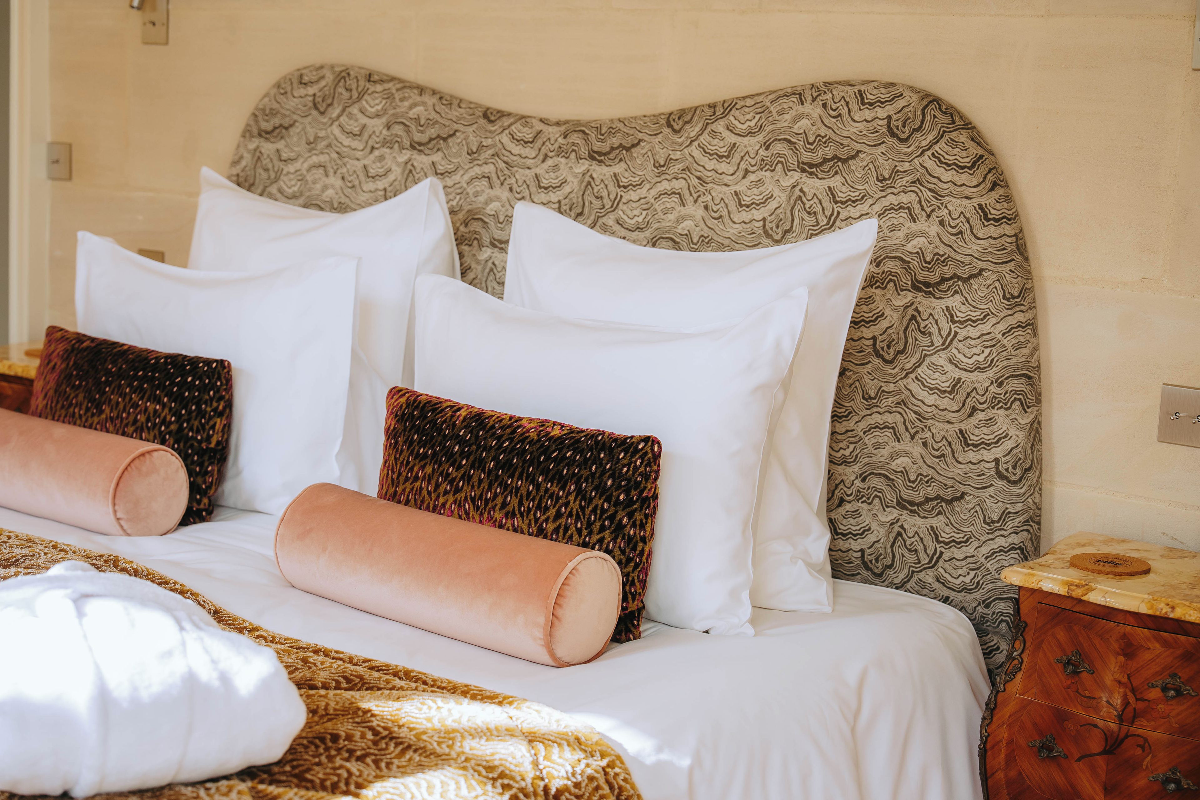 Un letto ben rifatto con lenzuola bianche, una testiera decorata e cuscini ornamentali.
