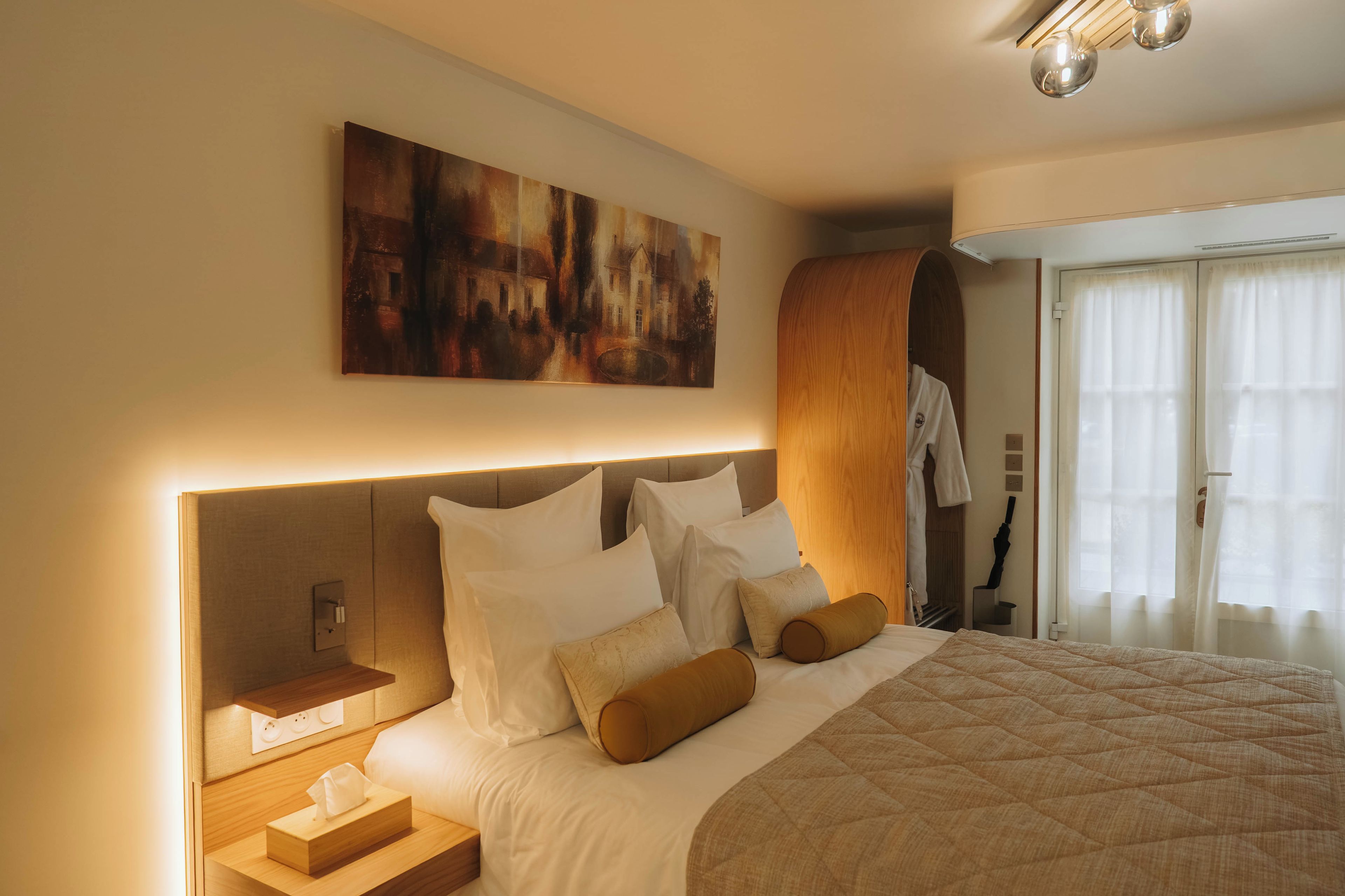 Una habitación de hotel con una cama grande, una mesita de noche con lámpara, un cuadro en la pared y un armario de madera.