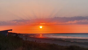 Une plage au coucher du soleil, avec un ciel dégagé, un horizon bien visible et une structure sur la gauche.