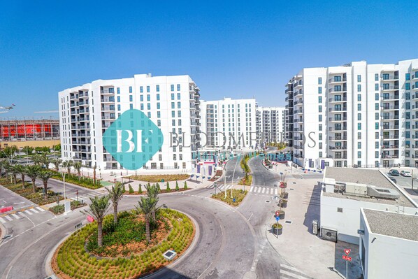 A modern apartment complex with multiple high-rise buildings, a roundabout, and landscaped areas with palm trees.