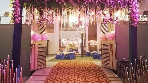 Un área de recepción con un arco floral, una alfombra estampada y un espacio de descanso con mesas y sillas.
