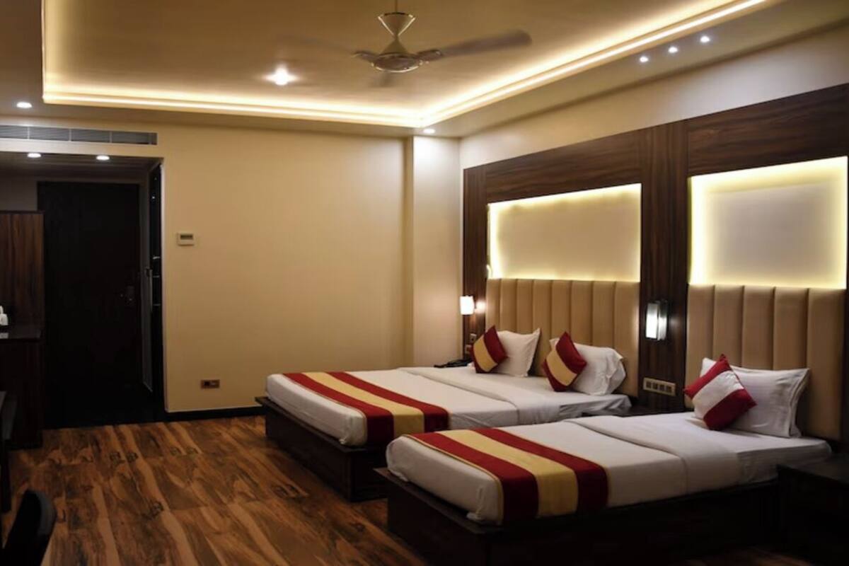 A hotel room with two beds, wooden flooring, a ceiling fan, and a TV on a stand.