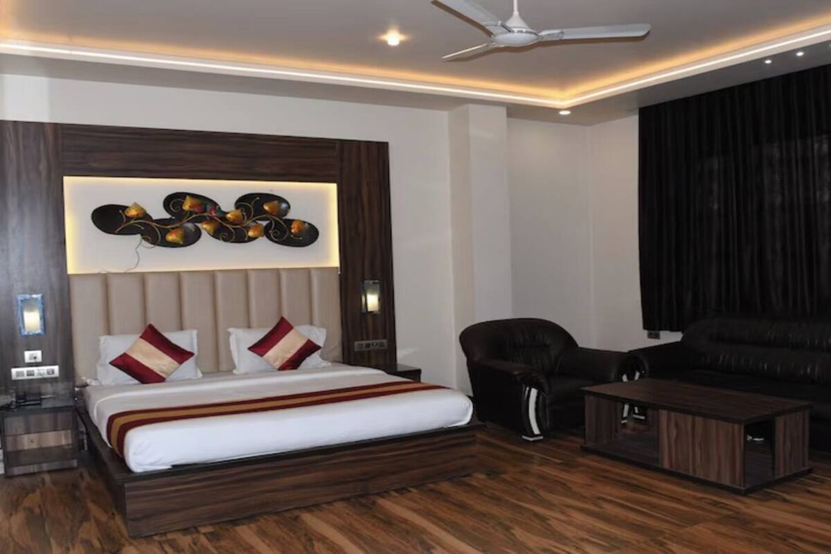A modern hotel room with a large bed, a sofa, a coffee table, and a ceiling fan.
