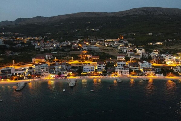 A coastal town at dusk with buildings along the waterfront, boats in the water, and a mountainous backdrop. - Seaside Escape, Podstrana (Podstrana)