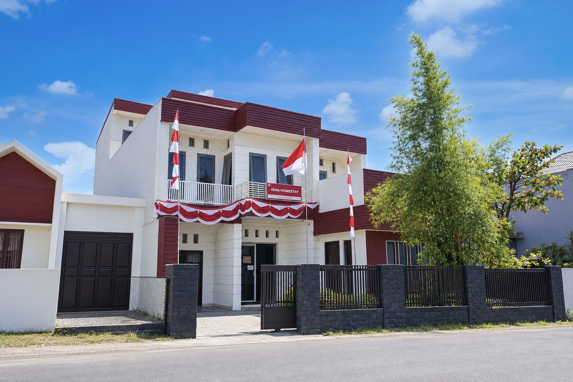 Um edifício de dois andares com varanda, uma bandeira e uma placa que diz 'IGHA HOMESTAY'.