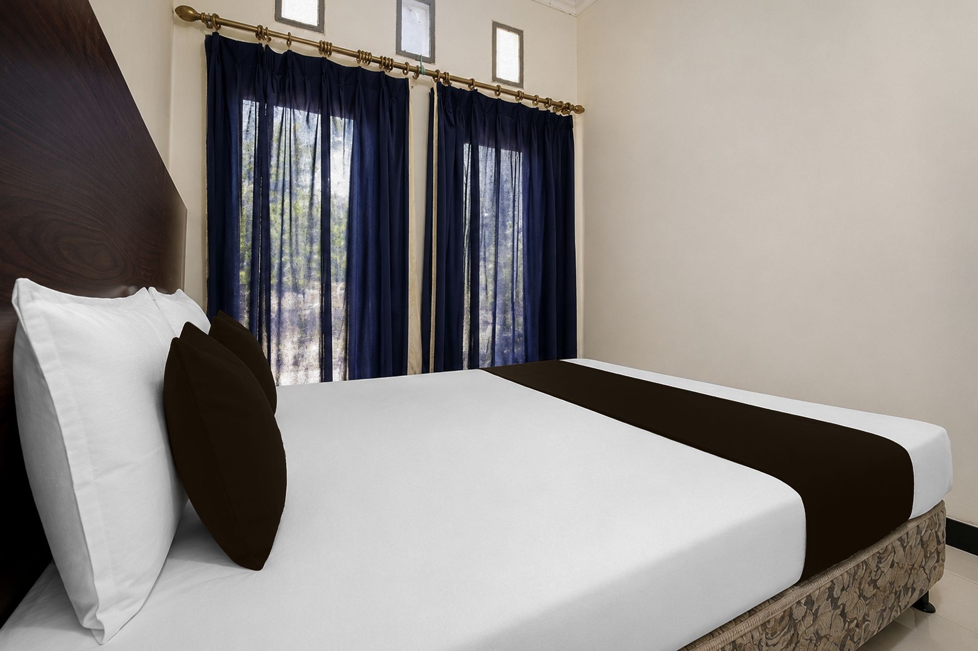 Una habitación de hotel con una cama, dos ventanas con cortinas y vistas a árboles.
