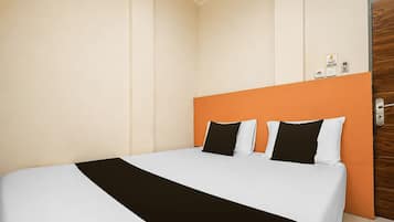 A hotel room with a bed, a wooden door, and a wall-mounted thermostat.