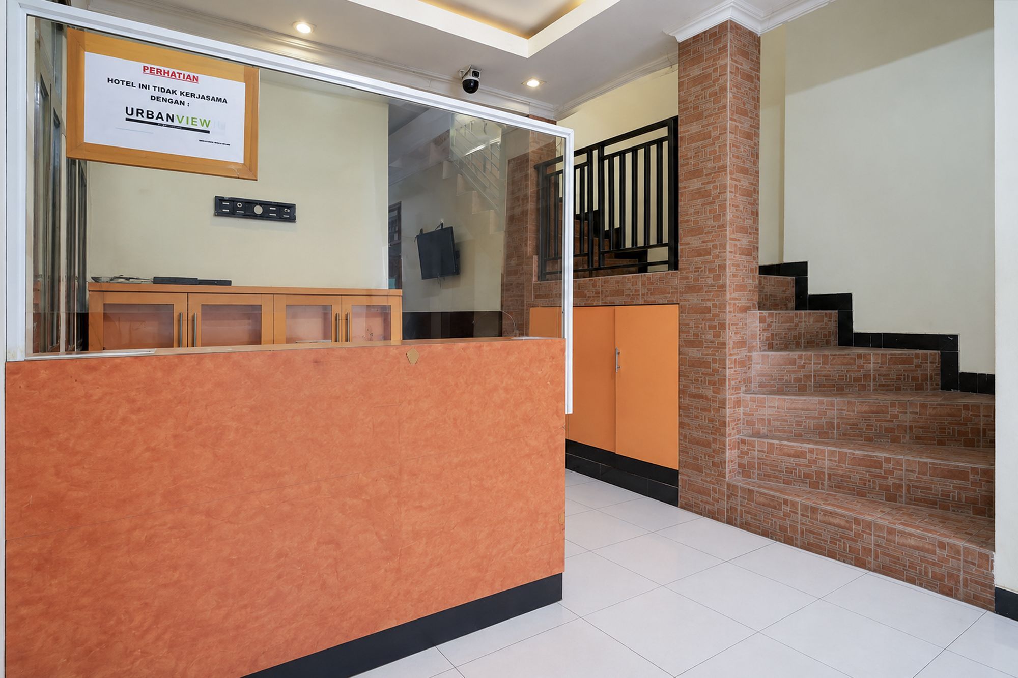 A reception area with a reception desk, a security camera, and a staircase with a brick wall.