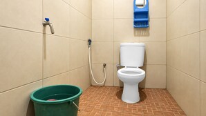 A small bathroom with a toilet, a green bucket, and a blue hand dryer on the wall. - Hotel O Icha Homestay (Makassar)