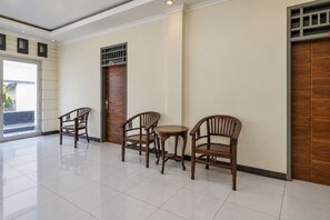 A hotel lobby with a tiled floor, wooden chairs, a small round table, and a door with a security panel. - Hotel O Icha Homestay (Makassar)