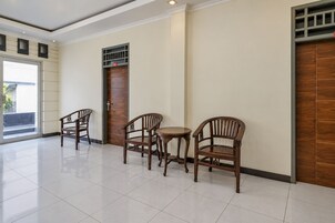 Vestíbulo de hotel con suelo de baldosas, sillas de madera, una pequeña mesa redonda y una puerta con panel de seguridad.
