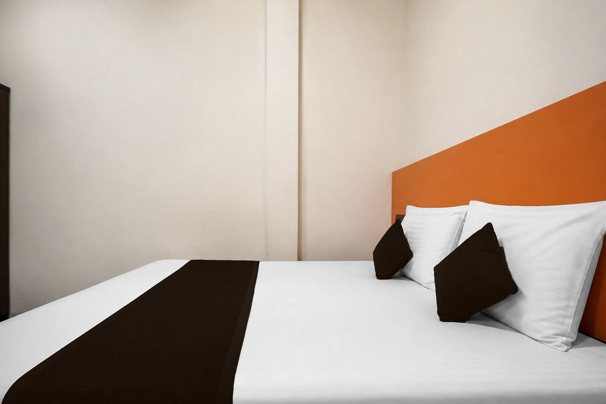 Una habitación de hotel con una cama, ropa de cama blanca, un plaid marrón y almohadas negras.