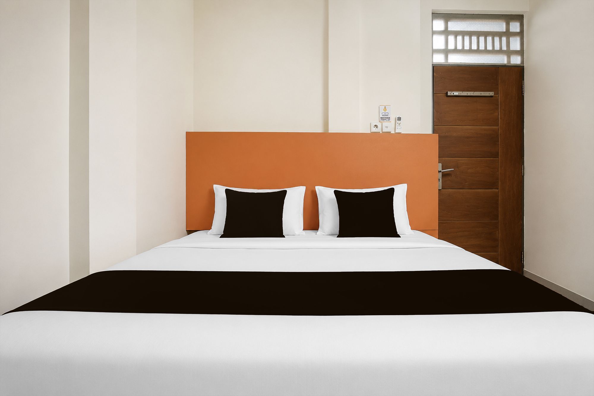 Quarto de hotel com cama, porta de madeira e janela pequena.