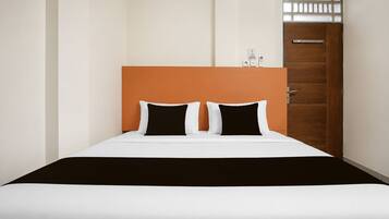 Quarto de hotel com cama, porta de madeira e janela pequena.