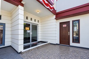 Un edificio con entrada de vidrio, zona de acceso con suelo de piedra y puerta de madera con un letrero.