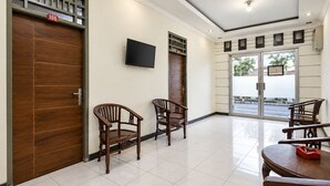 A hotel lobby with wooden doors, a flat-screen TV, and a seating area with chairs and a table. - Hotel O Icha Homestay (Makassar)