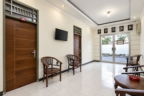 Um saguão de hotel com portas de madeira, uma TV de tela plana e uma área de estar com cadeiras e uma mesa.