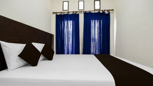 A hotel room with a bed, white bedding, a dark headboard, and blue curtains. - Hotel O Icha Homestay (Makassar)