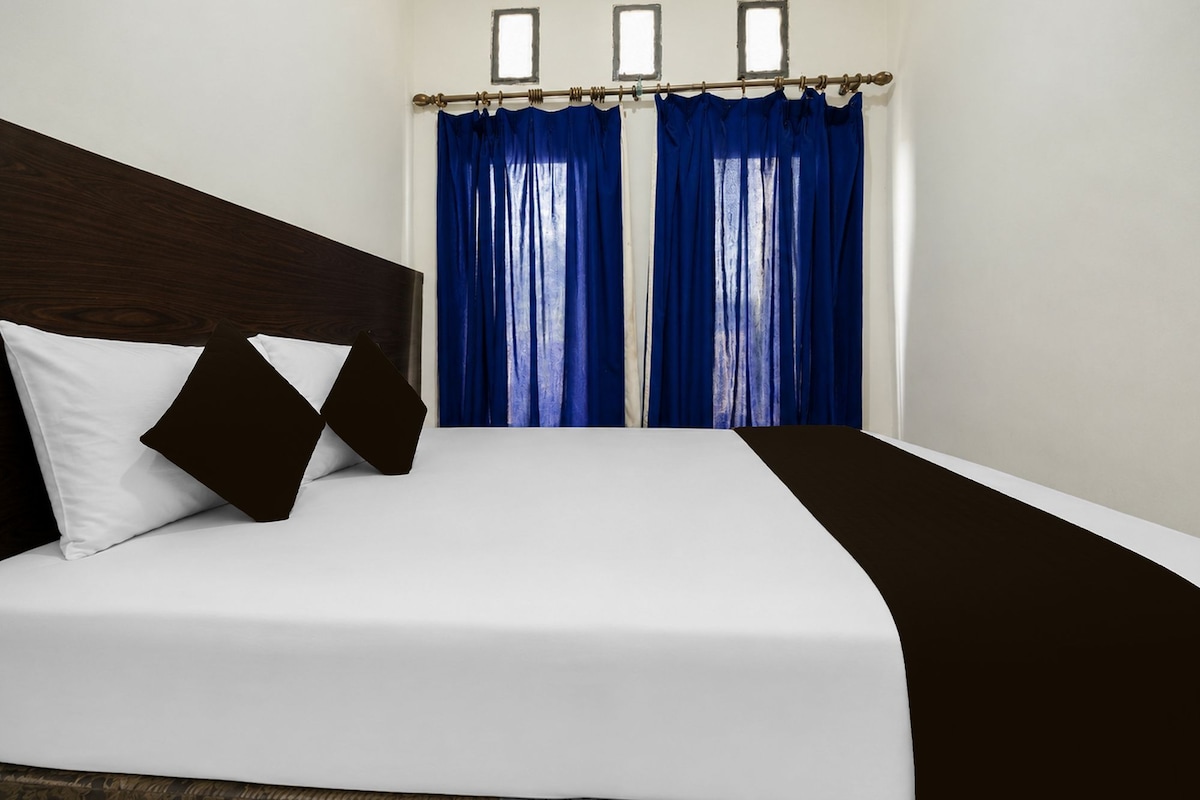 A hotel room with a bed, white bedding, a dark headboard, and blue curtains.