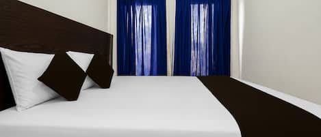 A hotel room with a bed, white bedding, a dark headboard, and blue curtains.